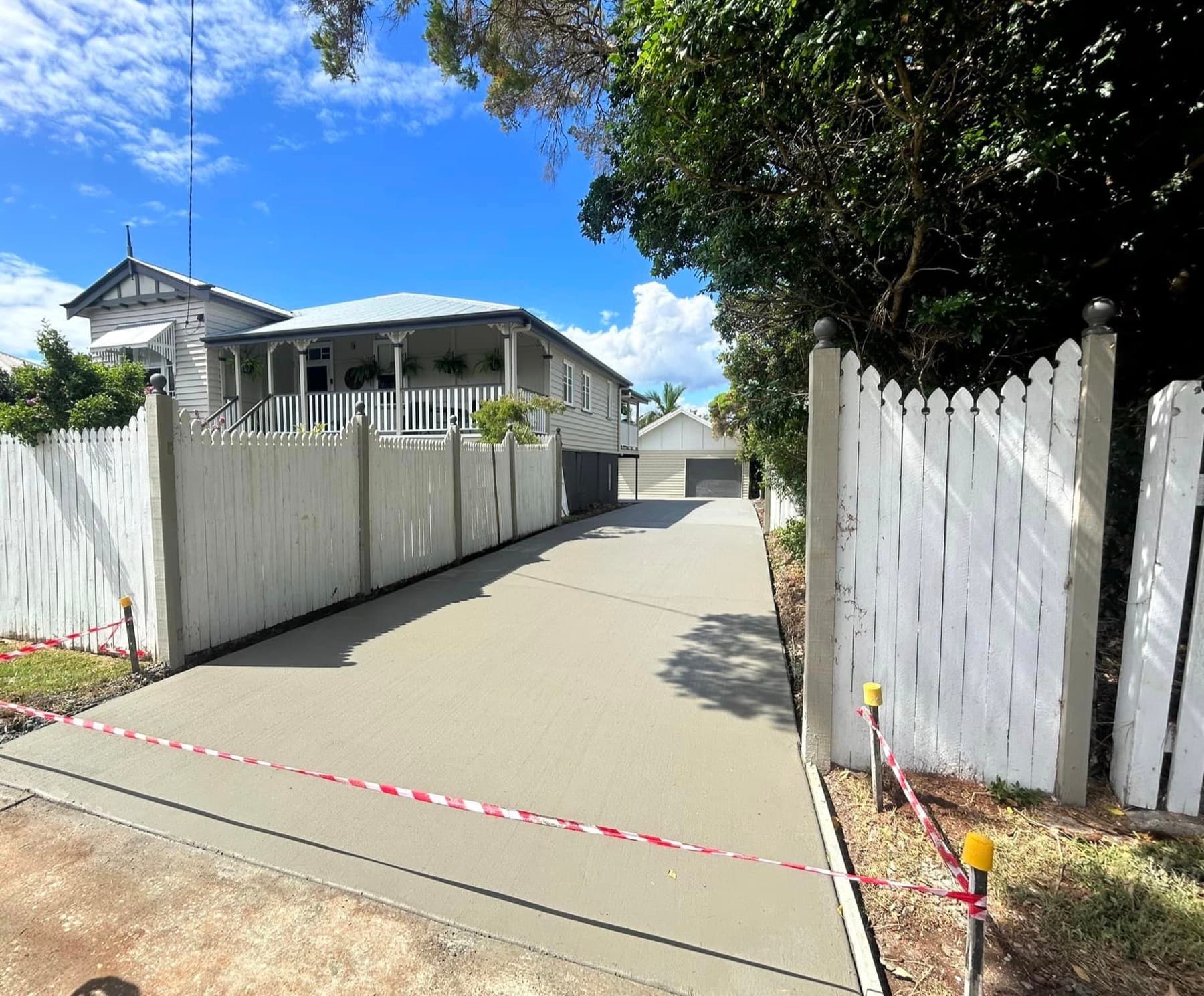 A long, freshly finished concrete driveway running past a white picket fence to a Queenslander