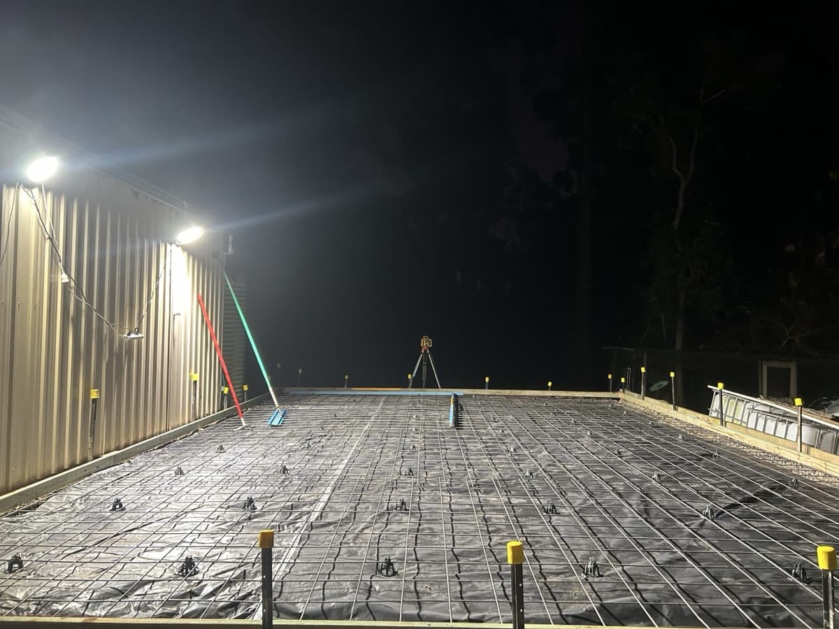 Steel reinforcement mesh laid in formwork beside a shed, lit at night